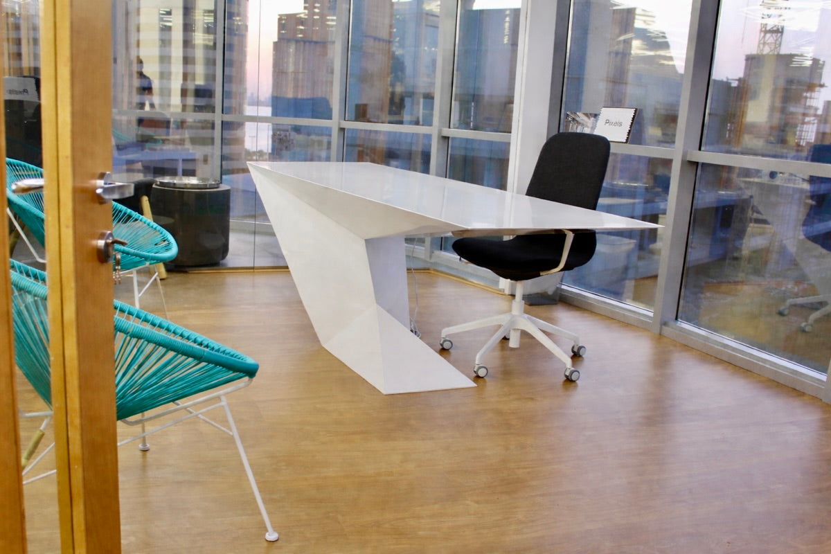 Modern office desk with chairs in a room with large windows overlooking a cityscape.